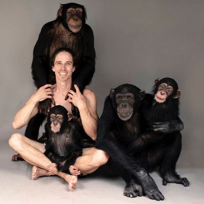 He is surrounded by four chimps with the baby sitting on his lap.
